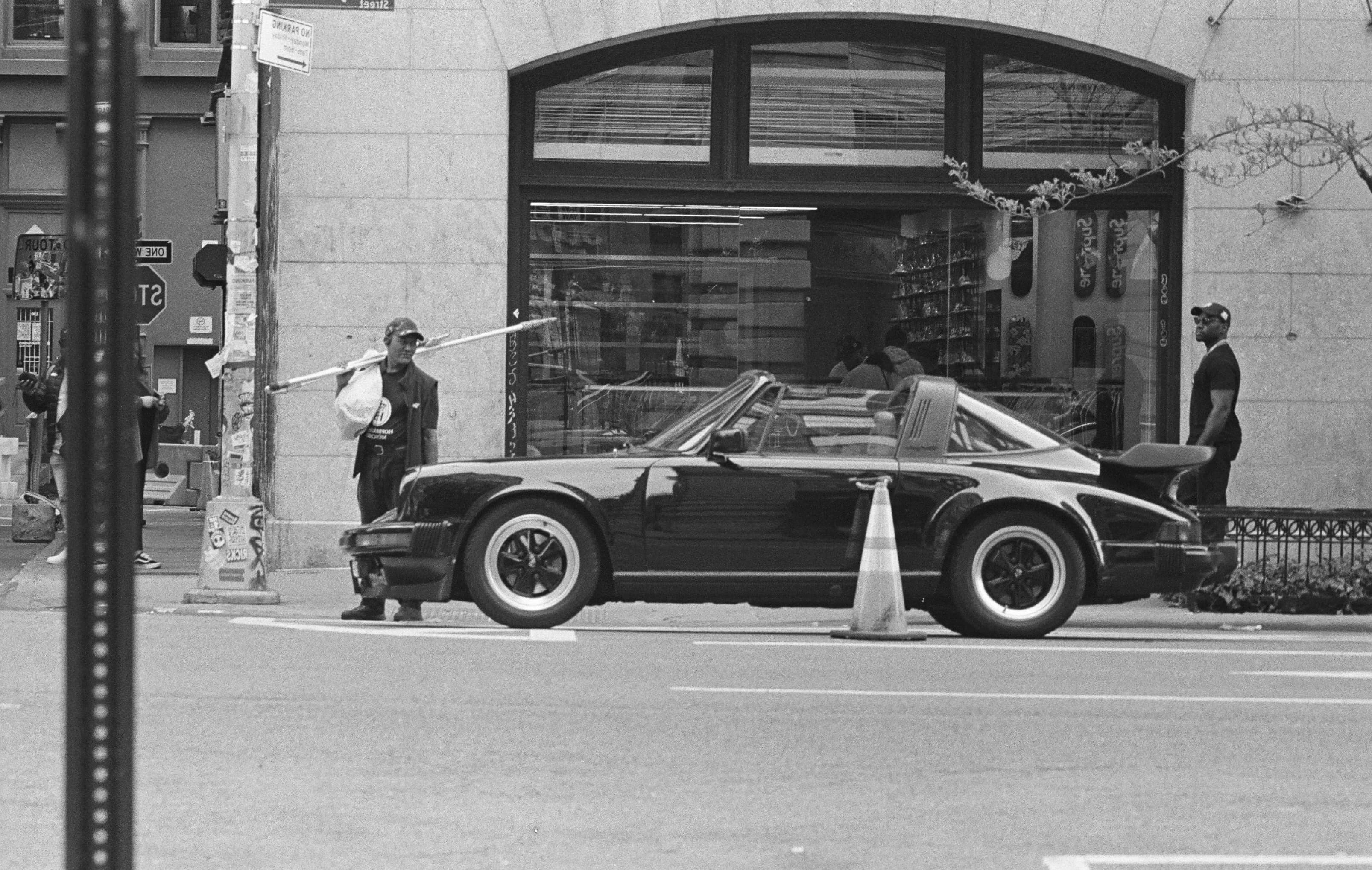 Man in NYC holding window cleaning tools looking at a black Porsche.